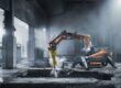 Orange bilningsrobot med hydraulikhammare i en dammig betongbyggnad