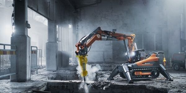 Orange bilningsrobot med hydraulikhammare i en dammig betongbyggnad