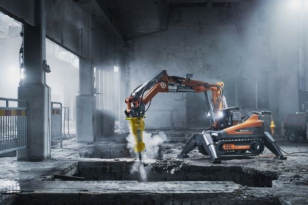 Orange bilningsrobot med hydraulikhammare i en dammig betongbyggnad