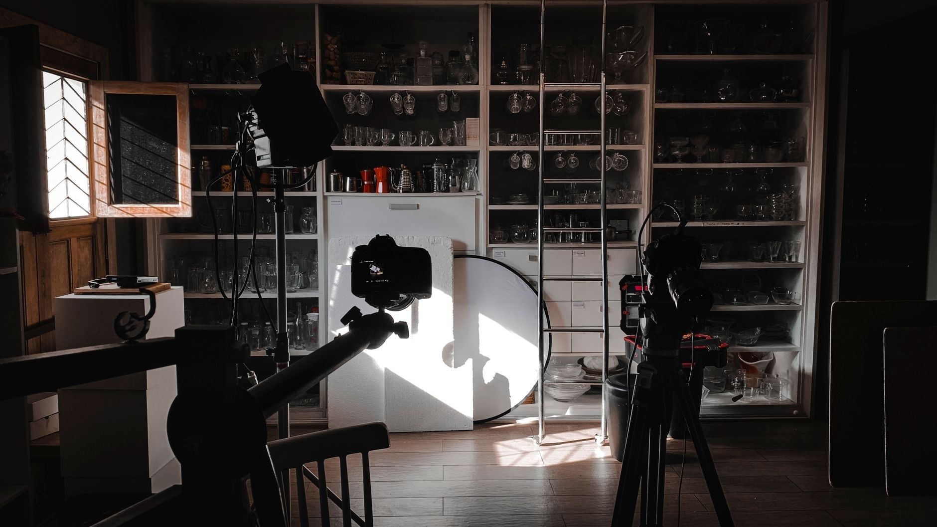 Fotoutrustning och reflektorskärm i fönusljus framför hyllor med glas